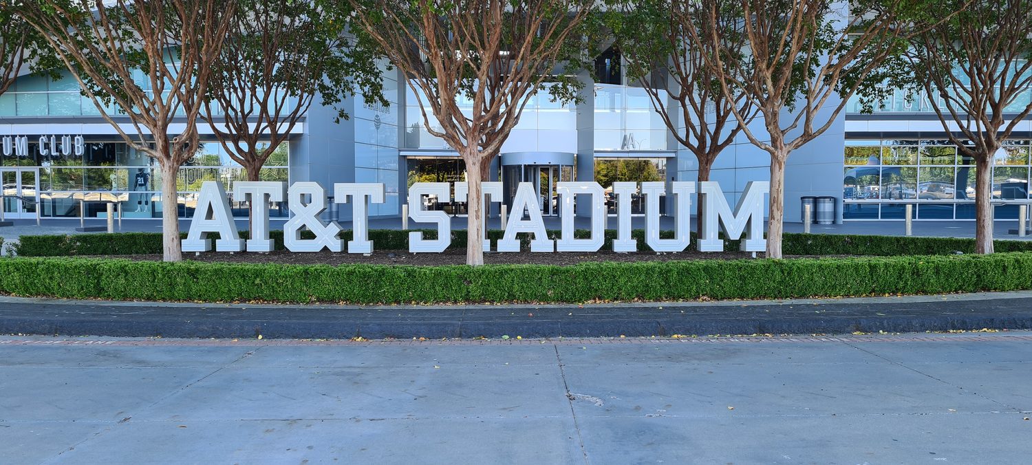 Der Schriftzug AT&T STADIUM vor dem Eingang, umgeben von Bäumen